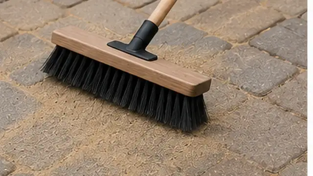 Person brushing soil and debris out of cleaned joints between patio pavers.