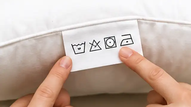 Person checking the care label on a yellow-stained pillow before cleaning it.