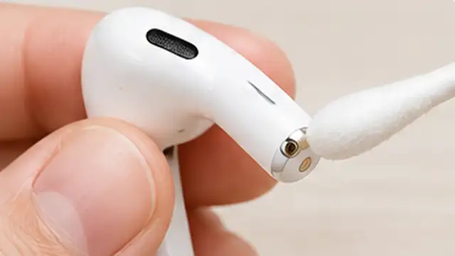 Person cleaning earbud charging contacts with a dry cotton swab and the case port with a soft dry brush.