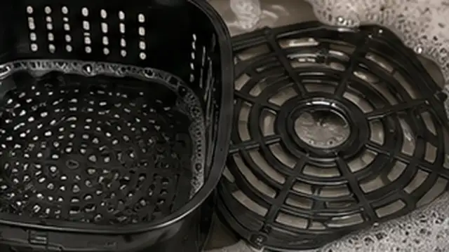 Person gently scrubbing softened food residue from a soaked air fryer basket with a soft nylon brush.