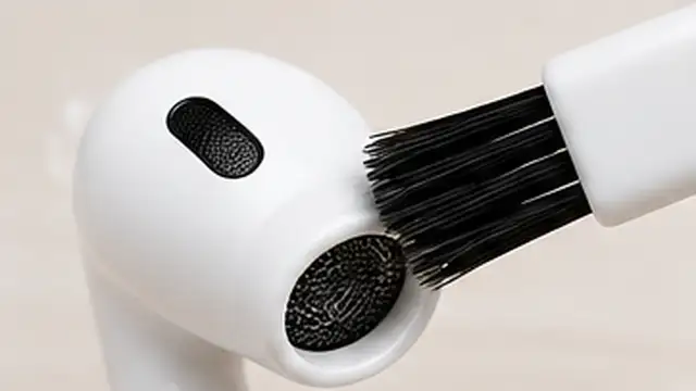 Person holding an earbud speaker mesh downward while gently brushing earwax away with a soft dry brush.