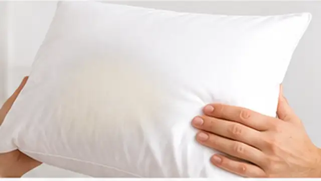 Person removing a pillowcase and inspecting yellow stains on the pillow underneath.