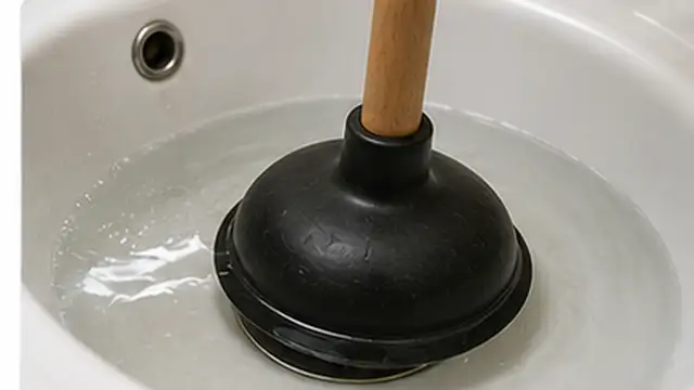 Person removing visible hair and debris from an open drain after lifting the stopper.