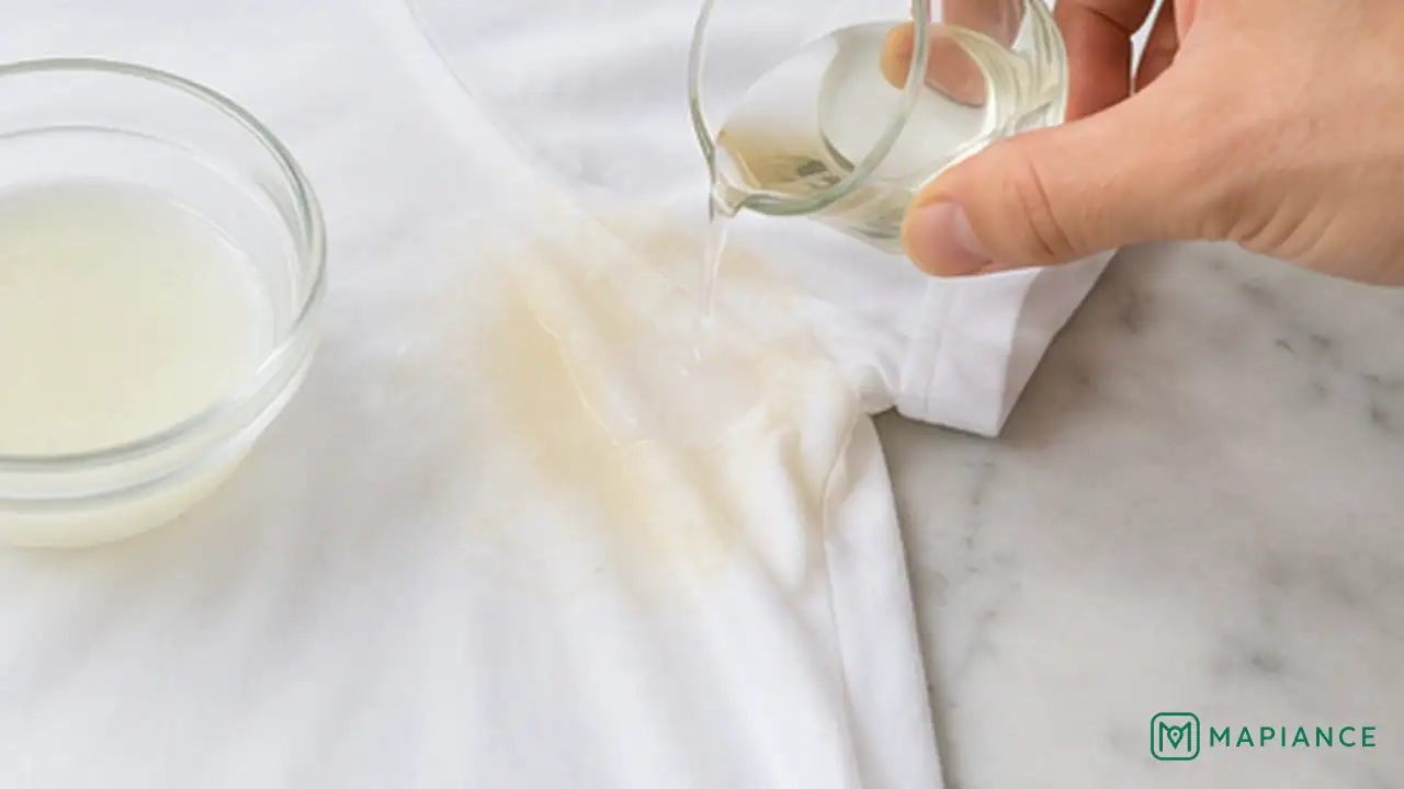 Person rinsing the back of a yellow underarm sweat stain on a white shirt with cool water.